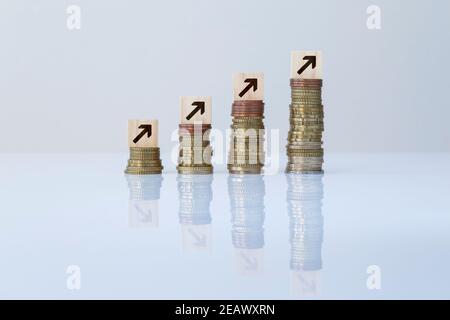 Frecce su blocchi di legno in cima a pile di monete ascendenti su sfondo grigio. Foto concettuale di economia, affari, finanza e crescita finanziaria. Foto Stock