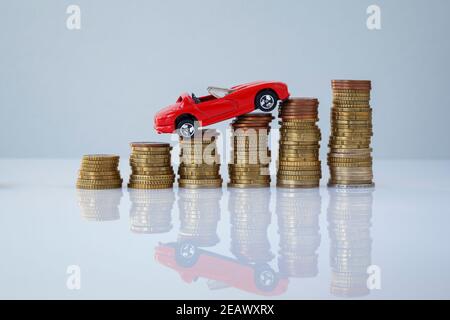Auto giocattolo rossa su pile di monete ascendenti su sfondo grigio. Foto concettuale di prestito auto e finanza, risparmio di denaro per un'auto, assicurazione e investimento. Foto Stock