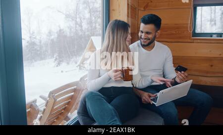 Felice giovane coppia che gode di vacanza invernale. Navigare sui social media su un computer portatile e bere bevande calde. Foto di alta qualità Foto Stock