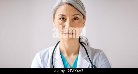 Ritratto panoramico di una dottoressa, medico o pediatra asiatica con capelli grigi in uniforme medica e stetoscopio, in piedi contro l'isola Foto Stock