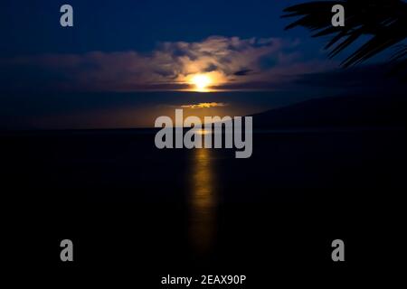 Ambiente lunare sull'oceano al mattino presto con luce arancione dorata che si riflette sull'oceano nella tropicale Hawaii. Foto Stock