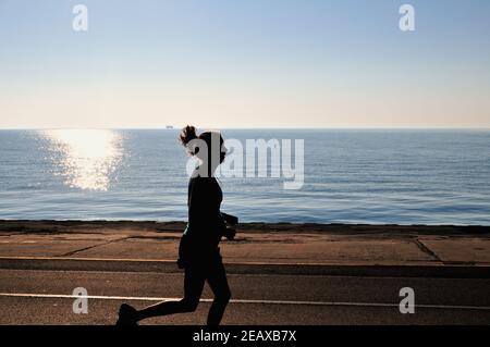 Chicago, Illinois, Stati Uniti. Una donna solitaria jogger è silhouette contro il riflesso del sole che sorge sul lago Michigan vicino North Avenue Beach. Foto Stock
