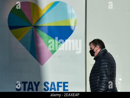 Dublino, Irlanda. 10 Feb 2021. Un uomo che indossa una maschera facciale cammina da un poster che dice 'stay strong' in una vetrina nella zona di Dún Laoghaire a Dublin.Ireland ha finora confermato 205,000 casi di Coronavirus con 23,364 recuperati e 3,752 morti. Credit: SOPA Images Limited/Alamy Live News Foto Stock