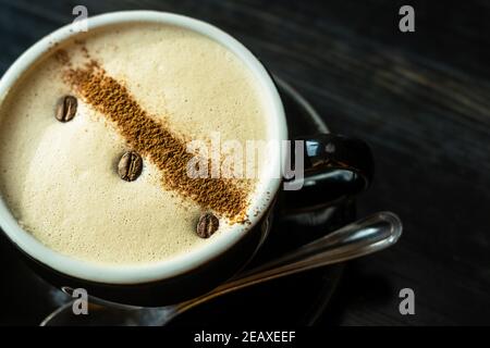 Una tazza di caffè con belle opere d'arte dai chicchi di caffè su uno sfondo scuro di legno. Foto Stock