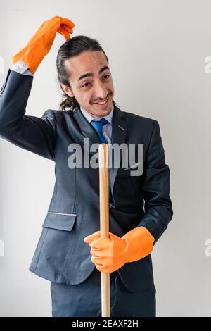 uomo d'affari in abito blu graffiando la testa per non sapere che cosa fare con i rifornimenti di pulizia che sta tenendo Foto Stock