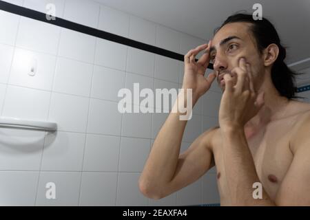 uomo esfoliante il viso in bagno, con due dita, anello e dita centrali Foto Stock