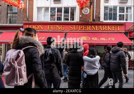 La gente che indossa le maschere facciali come misura preventiva contro la diffusione della coda di covid-19 nel negozio cinese di fronte a China Town, London.Chinese New Year è il più grande festival in Asia. Ogni anno, centinaia di migliaia di persone solitamente discendono sul West End di Londra per godere di una sfilata colorata, spettacoli di palcoscenico libero e piatti tradizionali cinesi, e per augurarsi a vicenda 'Xin Nian Kuai le' (Felice anno nuovo in Mandarino) o 'San Nin Faai Lok' (in Cantonese). A causa delle restrizioni nazionali di blocco, le persone possono godersi l'intrattenimento di Capodanno cinese di Londra da casa con una celebrazione online del passato C. Foto Stock