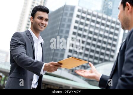 Uomo d'affari indiano che dà documento nella busta al suo asiatico partner esterno ufficio edificio in città Foto Stock