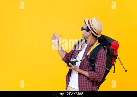 Felice uomo asiatico turista zaino in spalla indicando la mano per copiare spazio isolato a parte su sfondo giallo studio Foto Stock