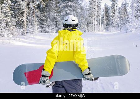 Donna snowboarder in tuta luminosa in un casco sportivo regge uno snowboard. Sport estremi. Tempo libero. Vista dal retro Foto Stock