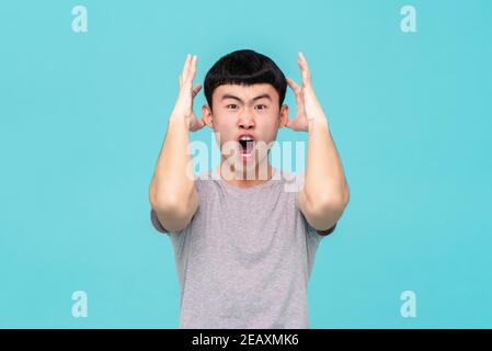 Aggressivo arrabbiato giovane asiatico emotivamente urlando isolato sulla luce sfondo blu studio Foto Stock