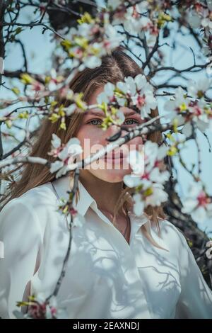 bella giovane donna nei raggi primaverili del sole tra i rami fioriti dell'albero Foto Stock