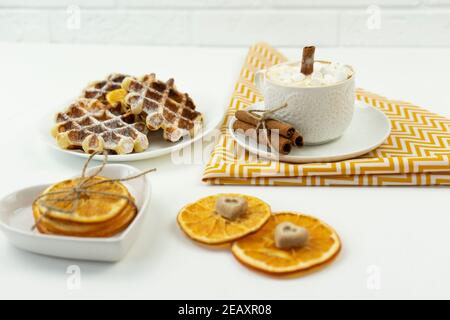 Prima colazione, caffè con marshmallows e un bastone di cannella E cialde belghe giacciono su un tavolo Foto Stock