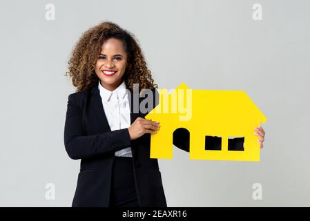 Attraente agente immobiliare afroamericano felice di tenere un giallo contenitore in cartone isolato su sfondo grigio studio Foto Stock