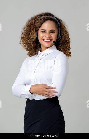 Le braccia sorridenti attraversavano la donna afroamericana indossando cuffie con microfono come uno studio del personale del call center ha girato su sfondo grigio chiaro Foto Stock