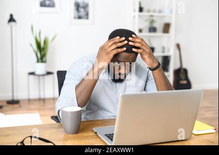 Testa girato serio perplesso afroamericano ragazzo sta guardando lo schermo del laptop. Il management esecutivo ha ricevuto cattive notizie in attesa di un positivo Foto Stock