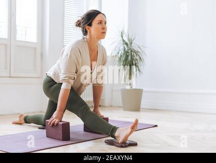 Bella donna bruna di mezza età in sportswear pactice yoga con attrezzature nello studio luci Foto Stock