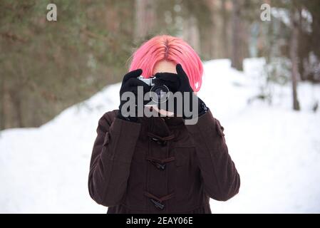 Donna con capelli rosa brillante con fotocamera retrò nella foresta invernale. Foto Stock