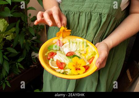 Donna che organizza fiori di nasturzio commestibili su insalata, cucina da giardino. Cibo vegano. Foto Stock