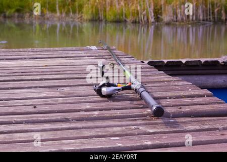 canna da pesca che giace su un ponte di legno vicino allo stagno Foto Stock