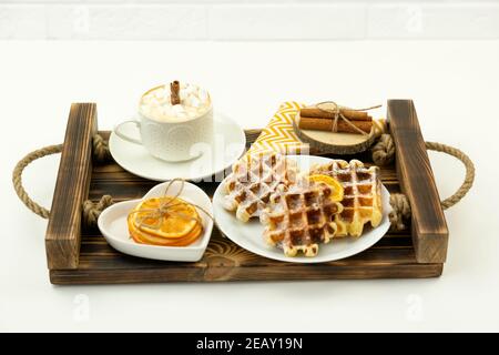 Prima colazione, caffè con marshmallows e un bastone di cannella E i waffle belgi giacciono su un vassoio di legno Foto Stock