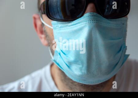 Faccia maschile in una maschera chirurgica blu e occhiali da sole neri Foto Stock