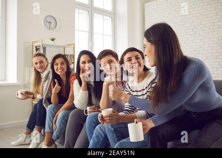 Donne felici che si siedono sul divano, bevono caffè, condividono buone notizie e si sostengono a vicenda