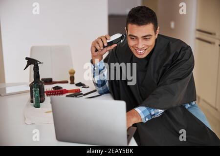 Bell'uomo che passa del tempo al computer con capelli diversi attrezzi negli appartamenti domestici Foto Stock