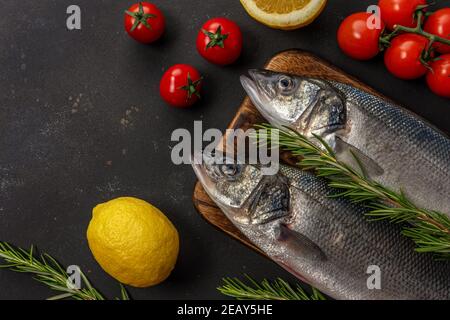 Due pesci di mare freschi con rosmarino e verdure su tavola nera. Concetto di pesce. Foto Stock