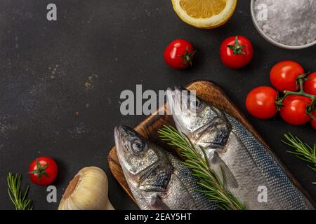 Due pesci di mare freschi con rosmarino e verdure su tavola nera. Concetto di pesce. Foto Stock
