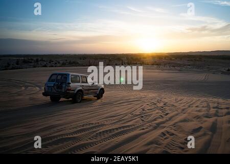 Tramonto colorato nel deserto. Un'auto fuoristrada si muove sulla sabbia nelle dune del deserto, sotto i raggi del sole che sorge. Foto Stock