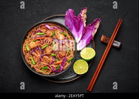 Pancit Bihon in ciotola nera su piano tavolo in ardesia scura. La cucina filippina spola il piatto con pancia di maiale, pollo, verdure. Cibo asiatico. Vista dall'alto Foto Stock