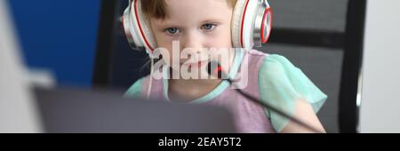 La bambina si siede al computer in cuffie con microfono Foto Stock