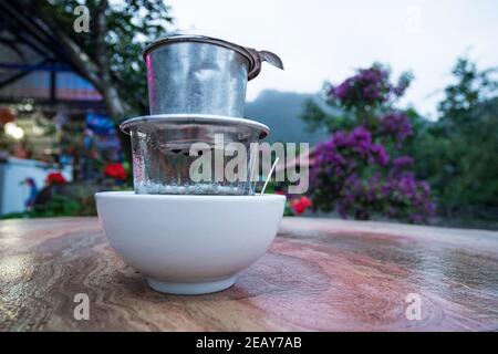 Caffè espresso in moka pot vecchia macchina da caffè, caffè caldo gocciolando in stile Vietnam. Prima colazione in natura sullo sfondo della montagna vietnamita l Foto Stock