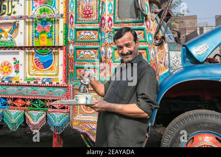 Lahore, Pakistan - Ottobre 2019: Uomo che beve tè vicino a camion colorato pakistano Foto Stock