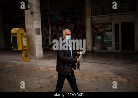 Athen, Grecia. 11 Feb 2021. Un uomo cammina lungo una strada di mercato indossando una copertura bocca-naso. Da giovedì mattina, la zona di Atene è stata nuovamente sotto un duro blocco per contenere la pandemia di Corona, con la polizia che ha fatto rispettare numerosi blocchi stradali. Credit: Angelos Tzortzinis/DPA/Alamy Live News Foto Stock