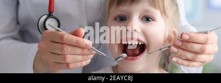 Dentista medico con stetoscopio esamina i denti di bambina in clinica Foto Stock