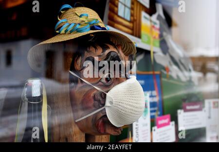 Farchant, Germania. 11 Feb 2021. Nella vetrina di una farmacia, una larva di legno, solitamente indossata dalla gente del posto durante la tradizionale passeggiata di Maschkera, indossa una maschera FFP2. Quest'anno, streghe, gnomi, campanili e altri personaggi del carnevale sono a casa - e così nella città alta bavarese di Farchant, figure con maschere storiche vi accolgono dalle finestre o dai balconi. Credit: Angelika Warmuth/dpa/Alamy Live News Foto Stock