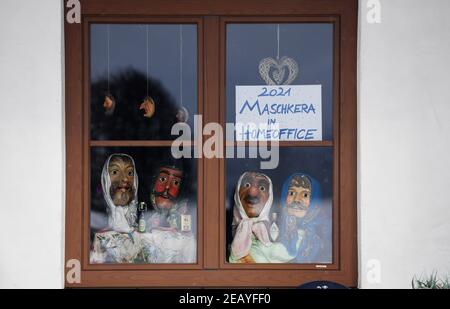 Farchant, Germania. 11 Feb 2021. In una finestra si possono vedere larve di legno, che la gente del posto indossa di solito durante la tradizionale passeggiata Maschkera, e un segno con l'iscrizione '2021 Maschkera nell'ufficio di casa'. Quest'anno, streghe, gnomi, campanili e altri personaggi del carnevale sono anche a casa - e così in Farchant in alta Baviera, figure con maschere storiche accolgono i visitatori dalle finestre o balconi. Credit: Angelika Warmuth/dpa/Alamy Live News Foto Stock