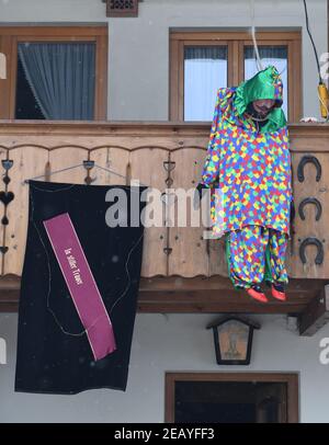 Farchant, Germania. 11 Feb 2021. 'In silenzio lutto' può essere visto su una tomba sash accanto a una tradizionale figura di carnevale appeso a una gatta, che la gente del posto di solito indossare durante il tradizionale Maschkera-Gehen, su una casa. Soggiornare a casa è anche il motto di quest'anno per streghe, gnomi, campanili e altri personaggi del carnevale - e così nella città alta bavarese di Farchant, figure con maschere storiche vi accolgono dalle finestre o balconi. Credit: Angelika Warmuth/dpa/Alamy Live News Foto Stock