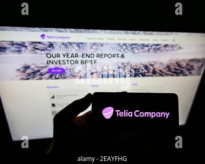 Persona che tiene lo smartphone con il logo del fornitore svedese di telecomunicazioni Telia Company AB sullo schermo di fronte al sito web. Mettere a fuoco il display del telefono. Foto Stock