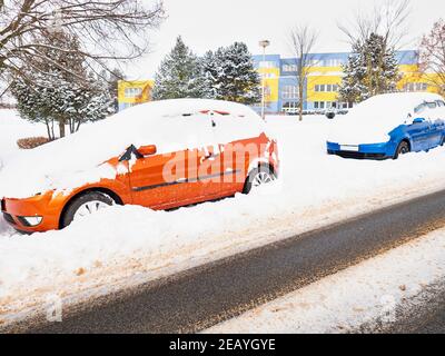 Auto abbandonate sepolte sotto una deriva di neve in inverno nel parcheggio. Case colorate in piano sullo sfondo Foto Stock