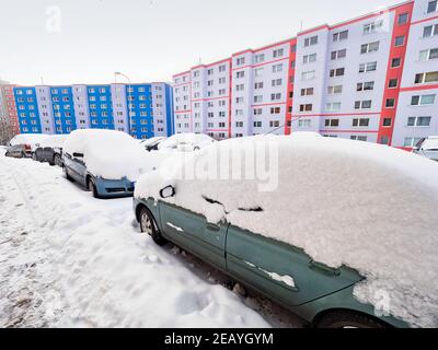 Auto abbandonate sepolte sotto una deriva di neve in inverno nel parcheggio. Case colorate in piano sullo sfondo Foto Stock