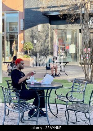 FRESNO, STATI UNITI - 10 febbraio 2021: Foto di due giovani seduti fuori dal centro commerciale seduti ai tavoli e rilassarsi in una giornata di sole Foto Stock