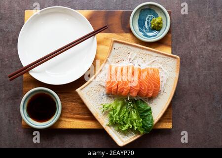 Sashimi di salmone con salsa di soia su riso con insalata presentata su una tavola di legno con bastoncini. Foto Stock