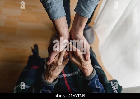 Vista dall'alto, giovane irriconoscibile che tiene le mani di una donna anziana. Anziani, cura, concetto di famiglia. Foto Stock