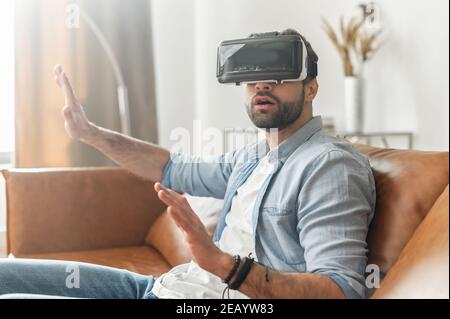 Un ragazzo impressionato che indossa occhiali con visore VR si chiede come il mondo virtuale sia realistico, un giovane uomo perso nella realtà virtuale, giocando a videogame, usando Foto Stock