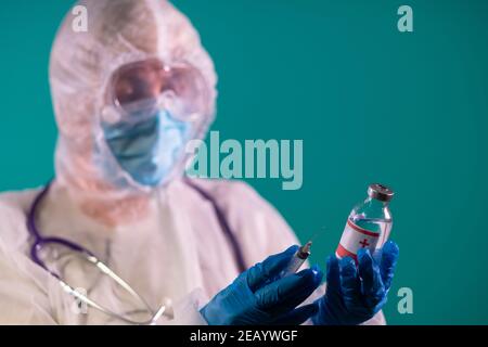 Medico femminile in tuta PPE con stetoscopio La spalla contiene una siringa e un vaccino COVID-19 guanti in nitrile blu Foto Stock