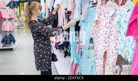 Donna sceglie i vestiti del bambino nel deposito. Messa a fuoco selettiva. Negozio. Foto Stock