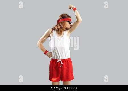 Nerd divertente skinny in canotta e shorts baciare debole bicipite dopo il primo allenamento sportivo Foto Stock